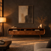 Low tv stand with pill shaped ends, three open cubbies and slim tapered legs in a dark living room at golden hour