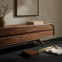 Corner detail of mid century TV console with a rounded open end on splayed legs beside wood, brass and linen samples