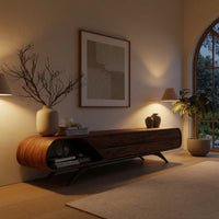 Mid century TV console with a rounded open end on splayed legs in an evening room lit by two lamps