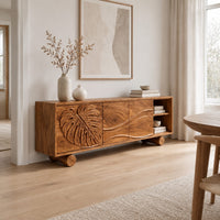 Sideboard with a carved monstera leaf door and an open end shelf in a Scandinavian dining room with white walls