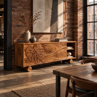 Sideboard with a carved monstera leaf door and an open end shelf in an industrial loft dining room with exposed brick