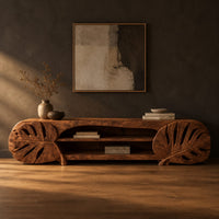 Long tv stand with monstera leaf carved ends and open shelves in the center in a dark studio against a charcoal plaster wall