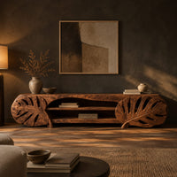 Long tv stand with monstera leaf carved ends and open shelves in the center in a dark living room at golden hour
