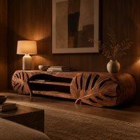 Long tv stand with monstera leaf carved ends and open shelves in the center in an evening living room with walnut wall paneling