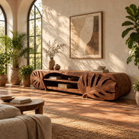 Long tv stand with monstera leaf carved ends and open shelves in the center in a bright living room with arched windows and plants