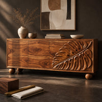 Corner detail of sideboard with a carved monstera leaf on the right doors and ball feet beside wood, brass and linen samples