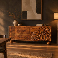 Sideboard with a carved monstera leaf on the right doors and ball feet in a dark dining room at golden hour