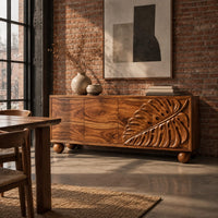Sideboard with a carved monstera leaf on the right doors and ball feet in an industrial loft dining room with exposed brick