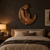 Carved wooden mother and child wall sculpture in a flowing crescent shape above a bed in a dusk lit bedroom