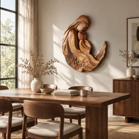 Carved wooden mother and child wall sculpture in a flowing crescent shape beside a dining table in natural light