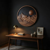 Round wooden mountain wall hanging with a black sky above a desk in a dark study corner