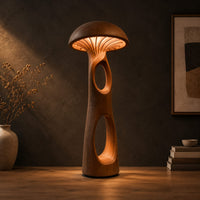 Mushroom floor lamp with a domed cap and tall carved stem in a dark studio against a charcoal plaster wall