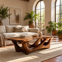 Natural edge coffee table with an open branching wood base in a bright living room with arched windows and plants