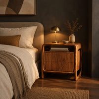 Nightstand with an open top cubby and a looped side frame in a dark bedroom at golden hour