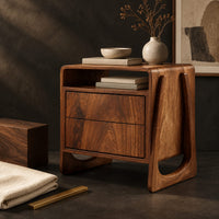 Corner detail of nightstand with an open top niche and sculpted loop shaped sides beside wood, brass and linen samples
