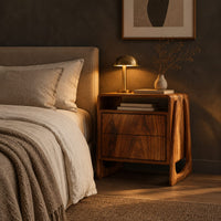 Nightstand with an open top niche and sculpted loop shaped sides in a dark bedroom at golden hour