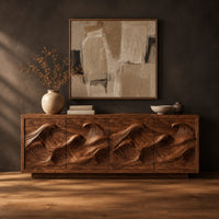 Low sideboard with four carved wave relief panels on a plinth base in a dark studio against a charcoal plaster wall