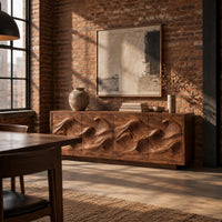 Low sideboard with four carved wave relief panels on a plinth base in an industrial loft dining room with exposed brick