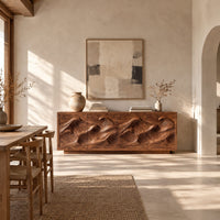 Low sideboard with four carved wave relief panels on a plinth base in a bright open plan dining room