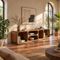 Low tv stand with soft edges and a stacked pair of oval cubbies in a bright living room with arched windows and plants