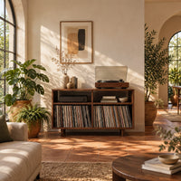 Open turntable stand with four square bays and short tapered legs in a bright living room with arched windows and plants