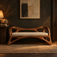 Wooden bench with a pale cushioned seat and an organic open frame in a dark entryway at golden hour