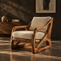 Armchair with a sculpted open wood frame and cream cushions, three-quarter view showing the grain