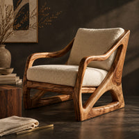 Corner detail of armchair with a sculpted open wood frame and cream cushions beside wood, brass and linen samples