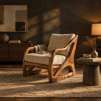 Armchair with a sculpted open wood frame and cream cushions in a dark living room at golden hour
