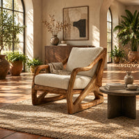 Armchair with a sculpted open wood frame and cream cushions in a bright living room with arched windows and plants