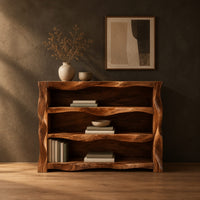 Open shelf console table with wavy sculpted sides in a dark studio against a charcoal plaster wall