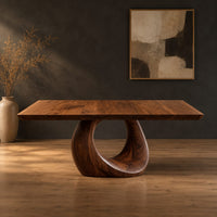 Dining table with a slab top and an open teardrop pedestal in a dark studio against a charcoal plaster wall