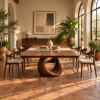 Dining table with a slab top and an open teardrop pedestal in a bright dining room with arched windows and plants