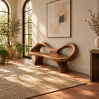 Organic wooden bench with a raised rim, two oval cutouts and tapered legs in a bright entryway with arched windows and plants