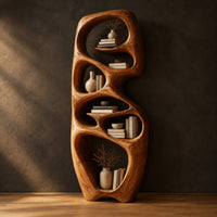 Tall organic wooden bookshelf with uneven oval shelf pockets in a dark studio against a charcoal plaster wall