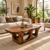Coffee table with round porthole openings in a solid base in a bright living room with arched windows and plants