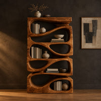 Stacked bookshelf with flowing teardrop shaped openings in a dark studio against a charcoal plaster wall