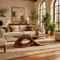 Oval coffee table on a twisting ribbon base with an open loop in a bright living room with arched windows and plants