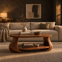 Oval coffee table with swelling tulip shaped legs and a lower shelf in a dark living room at golden hour