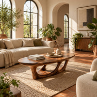 Oval coffee table with a sculpted open loop base in a bright living room with arched windows and plants