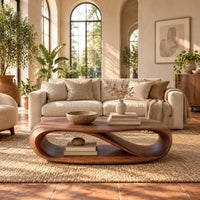 Oval coffee table with a twisting ribbon loop body and an open lower level in a bright living room with arched windows and plants