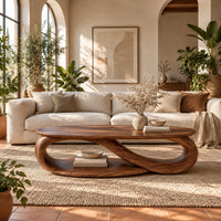 Oval coffee table with an infinity loop base and lower shelf in a bright living room with arched windows and plants