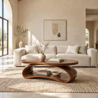 Oval wood coffee table on a looping ribbon base with an open lower shelf in a bright open plan living room