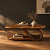 Oval coffee table with a low oval shelf and a single scroll support in a dark studio against a charcoal plaster wall