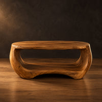 Oval coffee table with a sculpted body and open lower shelf in a dark studio against a charcoal plaster wall