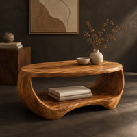 Corner detail of oval coffee table with a sculpted body and open lower shelf beside wood, brass and linen samples