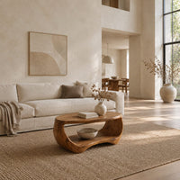 Oval coffee table with a sculpted body and open lower shelf in a bright open plan living room