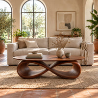 Oval coffee table with a sculpted infinity loop base in a bright living room with arched windows and plants