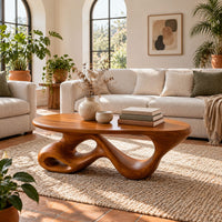 Oval coffee table on a twisting ribbon base with open loops in a bright living room with arched windows and plants