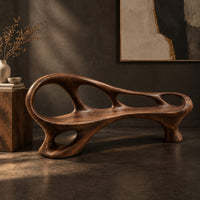 Corner detail of long wooden bench with oval cutouts along the back rail and a flowing frame beside wood, brass and linen samples